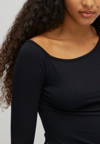 Black ribbed long-sleeve top with a wide neckline, made from a soft fabric, featuring a fitted silhouette and subtle side ruching detail.