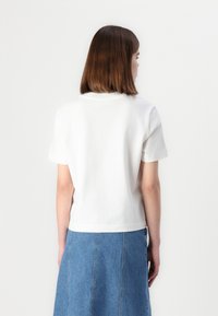 Hvit t-skjorte med korte ermer og rund hals, laget av bomull. Har en avslappet passform og et rent, enkelt design, kombinert med et denimskjørt.