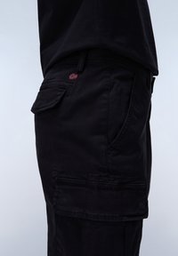 Black cargo pants featuring multiple pockets, a relaxed fit, and a small embroidered flag detail on the back pocket. Smooth fabric texture.
