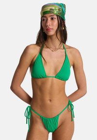 Φωτεινό πράσινο μπικίνι από απαλό ύφασμα· τοπ τρίγωνο με λεπτές τιράντες και μίνιμαλ κάτω μέρος με πιέτες.