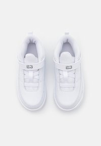 Bílé tenisky s polstrovaným límcem, síťovinovou podšívkou, prošívanými detaily a suchým zipem. Na popruhu je šedý štítek s číslem "23".