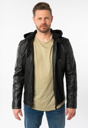 Schwarze Lederjacke mit abnehmbarer schwarzer Kapuze. Verfügt über Nähte und einen Reißverschluss. Wird über einem hellgrünen Hemd und blauen Jeans getragen.