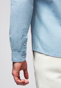 Manche de chemise en denim bleu clair avec un poignet boutonné et une quincaillerie argentée. Texture lisse, coupe décontractée, avec un ourlet droit.