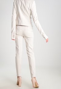 Blazer bianco aderente con design cropped e polsini con bottoni, abbinato a pantaloni bianchi su misura e tacchi alti beige. Texture liscia.