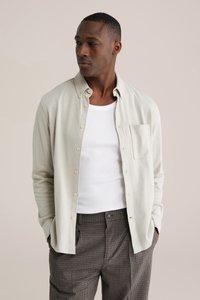 Šviesiai pilka marškinėliai su mažomis krūtinės kišenėmis, derinami su balta palaidine be rankovių ir rudomis languotomis kelnėmis, pasižyminčiomis laisvu siluetu.