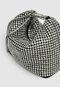 Srebrna torbica ukrašena rhinestones-ima, zaobljenog oblika, s crnom tkaninom kao osnovom i zatvaranjem na cipelu s metalnim hardverom. Tekstuirana površina.