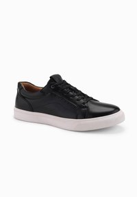 Baskets en cuir noir avec une semelle en caoutchouc blanche, bout rond, col rembourré et lacets plats. Surface lisse avec un détaillage minimal.