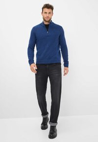Maglione lavorato a maglia blu con colletto a mezza zip, abbinato a jeans in denim scuro e scarpe nere con risvolti arrotolati. Design semplice e funzionale.
