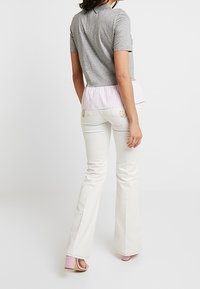 Top grigio a maniche corte con un orlo plissettato a righe rosa, abbinato a pantaloni bianchi a zampa d'elefante e scarpe rosa con tacco. Visto dal retro.