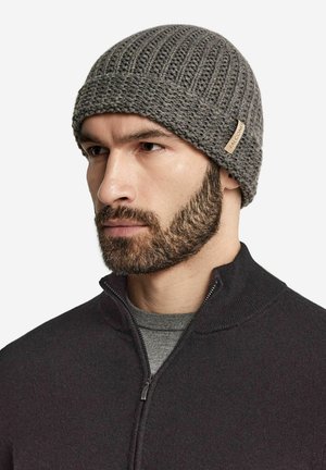 Berretto in maglia grigia con una texture a costine e un piccolo etichetta in tessuto. Indossato da una persona con una felpa scura con zip e una maglietta grigia.