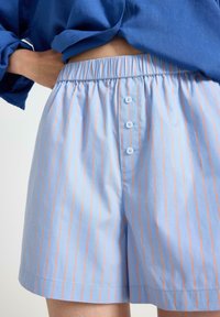 Lyseblå pyjamashorts med orange lodrette striber, elastisk talje og tre blå knapper foran. Glat stofstruktur.