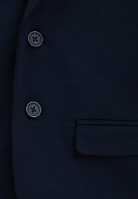 Marinblå kavajtyg med en slät textur, som har två svarta knappar och en liten, diskret ficka på vänster sida.