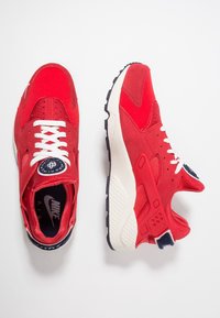 Ett par röda Nike Air-sneakers med vita snörningar, svart och vit sula, och logotyp på tungan, visade från ovan- och sidovy.