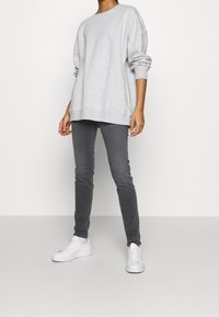 Sudadera de gran tamaño en gris claro con hombros caídos, combinada con jeans ajustados en gris oscuro y zapatillas blancas. Textura de algodón suave.