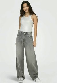 Blugi din denim gri cu picioare largi și talie legată, asortați cu un top alb ajustat și adidași albi. Textură netedă și stil casual.