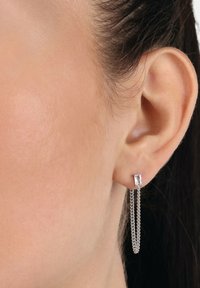 Oreja adornada con un pendientes de plata con una piedra rectangular, que cuenta con dos delicadas cadenas de plata que cuelgan hacia abajo.