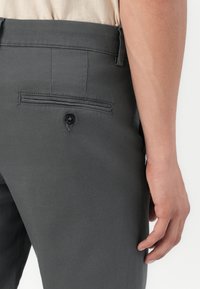 Pantalones de tejido gris con un bolsillo trasero con cierre de botón, textura suave y un corte entallado, mostrados de perfil.