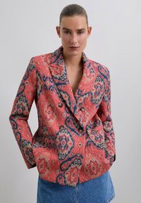 Blazer de corte doble en un rojo vibrante con intrincados patrones en azul y dorado, que presenta grandes botones y una tela texturizada.