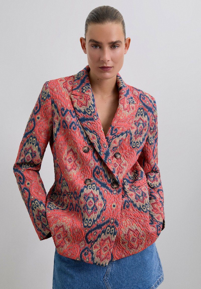 Blazer de corte doble en un rojo vibrante con intrincados patrones en azul y dorado, que presenta grandes botones y una tela texturizada.
