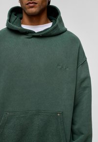 Groene hoodie met een gestructureerde capuchon, een voorklep met drukknopen en subtiele geborduurde branding. Zachte, relaxed fit.