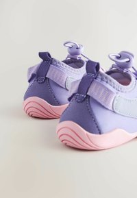 Baskets de sport violettes avec un dessus en tissu doux, semelles en caoutchouc roses et sangles ajustables avec fermeture à boucle. Talon profilé pour un soutien.