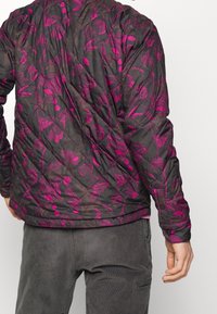 Svart vadderad jacka med ett livligt magenta-blomster mönster. Anmärkningsvärd textur och design med ståkrage och knappdetaljer.