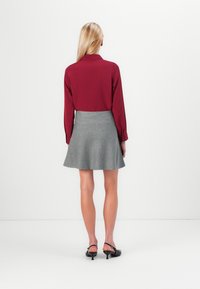 Röd långärmad blus med krage, ihop med en grå utsvängd kjol. Outfiten har en mjuk textur och en klassisk snitt. Svarta skor med rem.