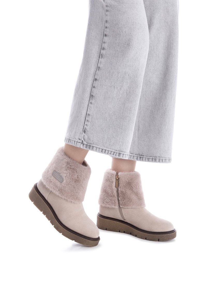 Botas de tobillo beige de ante con un suave cuello de piel de color rosa, cremallera lateral y suela de goma texturizada. Combinadas con un pantalón de mezclilla gris de pierna ancha.