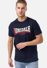 Marineblå bomulds t-shirt med et stort hvidt og rødt "LONSDALE LONDON" logo på forsiden; rund hals, korte ærmer.