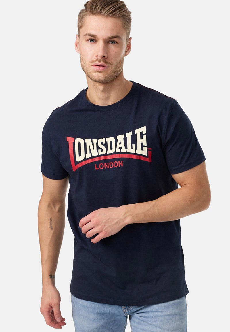 Marineblå bomulds t-shirt med et stort hvidt og rødt "LONSDALE LONDON" logo på forsiden; rund hals, korte ærmer.
