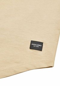 T-shirt in cotone beige con texture a coste, dotata di un'etichetta nera con testo bianco che include "JACK & JONES" e "EST. 1990."