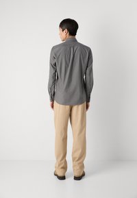 Camisa gris de manga larga con cuello, con una textura suave y puños con botones, combinada con pantalones beiges y zapatos negros.