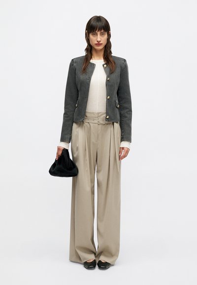 Giacca in denim grigio con bottoni dorati, abbinata a pantaloni beige a gamba larga e una borsa nera. L'outfit è completato da una maglietta bianca e ballerine nere.