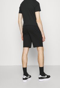 Černé tričko s krátkým rukávem spárované s černými šortkami a černými teniskami s bílými akcenty. Oblek má jednoduchý, neformální design.
