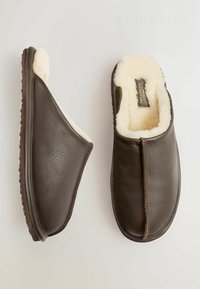 Brūnas ādas čības ar teksturētu virsmu un pūkainu krēmkrāsas oderi. Noapaļota forma ar atklātiem šuvēm un gumijas zoli labai saķerei.