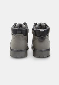 Pelēki pārgājienu apavi ar melniem akcentiem, izgatavoti no izturīgiem materiāliem. Iespējas ietver pastiprinātu papēdi, vidus teļa augstumu un teksturētu zoli, kas nodrošina saķeri.