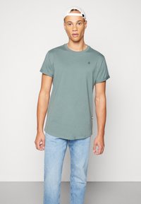 Camiseta de algodón verde con cuello redondo, mangas cortas y dobladillo recto. Presenta un pequeño logo en el pecho y un ajuste relajado.