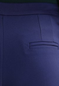 Marinblått tyg med en slät yta har en horisontell skärfickdetalj. Enkel design med skräddarsydda sömmar och inga synliga stängningar.