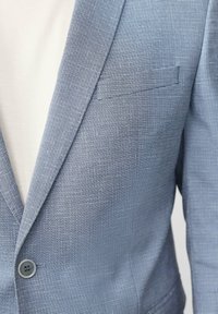 Blauer strukturierter Blazer mit dezentem Karomuster, Ein-Knopf-Verschluss und seitlicher Tasche. Der Stoff ist leicht und glatt.