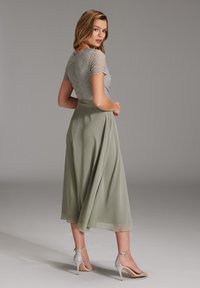 Abito con corpino in pizzo di colore verde chiaro, dotato di una gonna fluente e di una lunghezza alla caviglia. Tacchi a strappo argentati completano l'outfit.