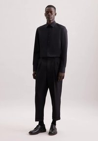 Camicia nera con bottoni, dal design corto e maniche lunghe, abbinata a pantaloni neri larghi e scarpe eleganti nere.