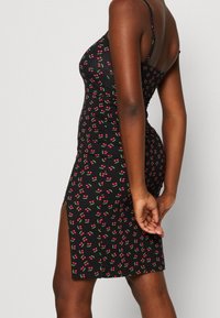 Schwarzes Kleid mit kleinem pinken Kirschmuster, figurbetontes Design, Spaghetti-Träger und seitlichem Schlitz. Dehnbare Stoffqualität mit glatter Textur.