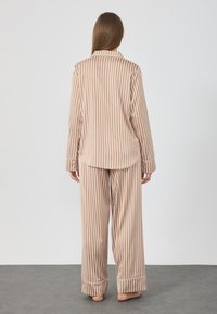 Pajama set so zlatohnedými a bielymi prúžkami, ktorý obsahuje košeľu s dlhým rukávom na gombíky a nohavice s širokými nohavicami, vyrobený z ľahkej, hladkej látky.