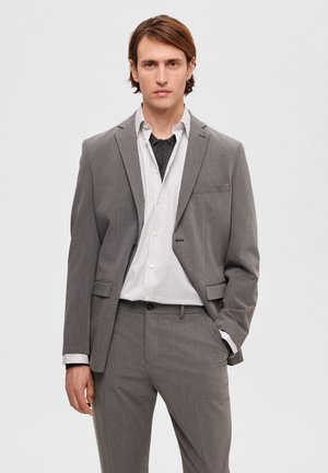 Traje gris de dos piezas con solapa muesca, ajuste slim, combinado con una camisa de botones a rayas blancas y grises. La tela parece texturizada.