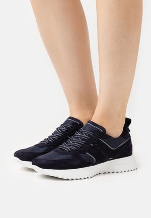 Baskets en daim bleu marine avec des accents sombres contrastés, des lacets blancs, et une semelle extérieure blanche texturée présentant un motif dentelé.