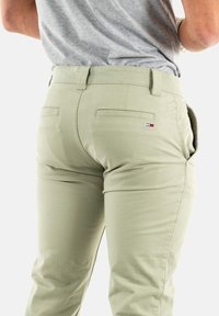 Jasnozielone spodnie o gładkiej teksturze, z tylnymi kieszeniami i małym logo w kolorach czerwonym, białym i niebieskim na pasku talii.