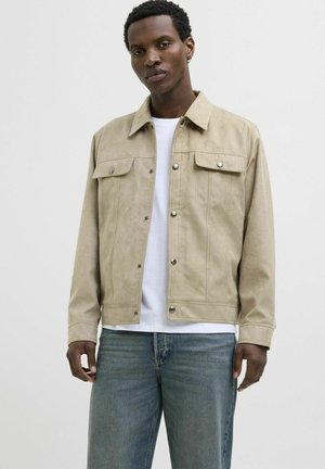 Beige suede jacket with a collared neckline, button closure, two chest pockets, and a fitted design, worn over a white t-shirt and jeans.