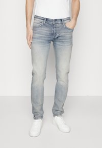 Jeans de mezclilla azul claro con un acabado desgastado, diseño de cinco bolsillos y corte recto, combinados con zapatillas blancas y una camisa blanca.