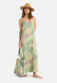 Abito maxi verde chiaro con motivi floreali in rosa, giallo e blu; spalline sottili; abbinato a una borsa tote coordinata.