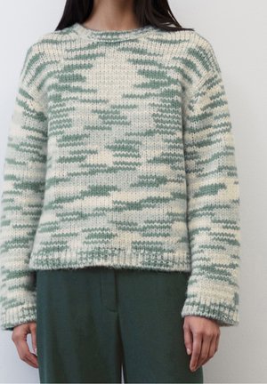 Pull en tricot crème avec un motif camouflage vert, doté d'un col rond et de poignets côtelés. Porté avec un pantalon vert assorti.